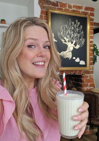 Artist Becky Wash drinks a banana milkshake in Nest with her Brentwood Art Trail piece, The Whomping WIllow, behind her.